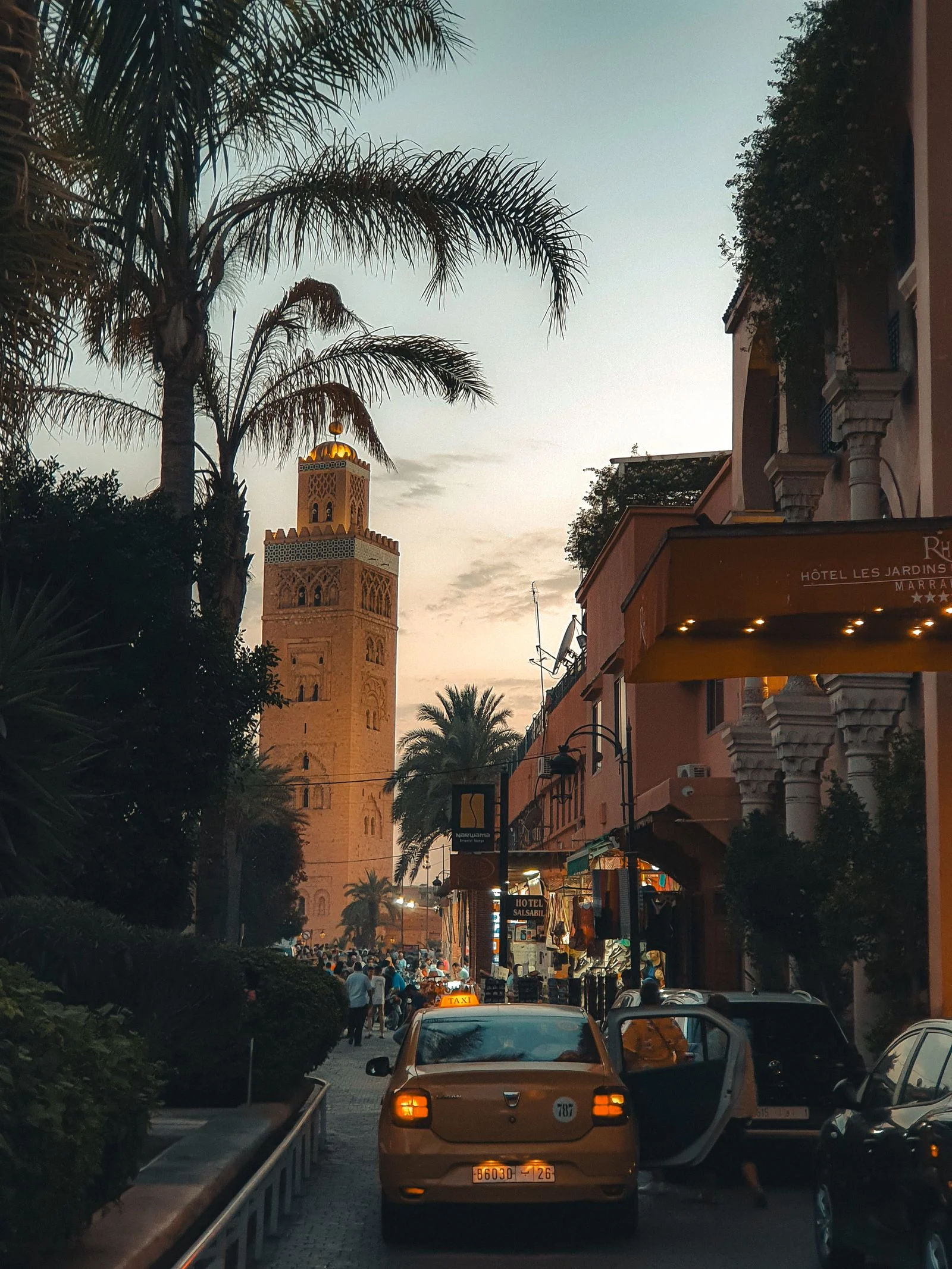 Bustling street scene in Marrakech at sunset with taxis and commuters