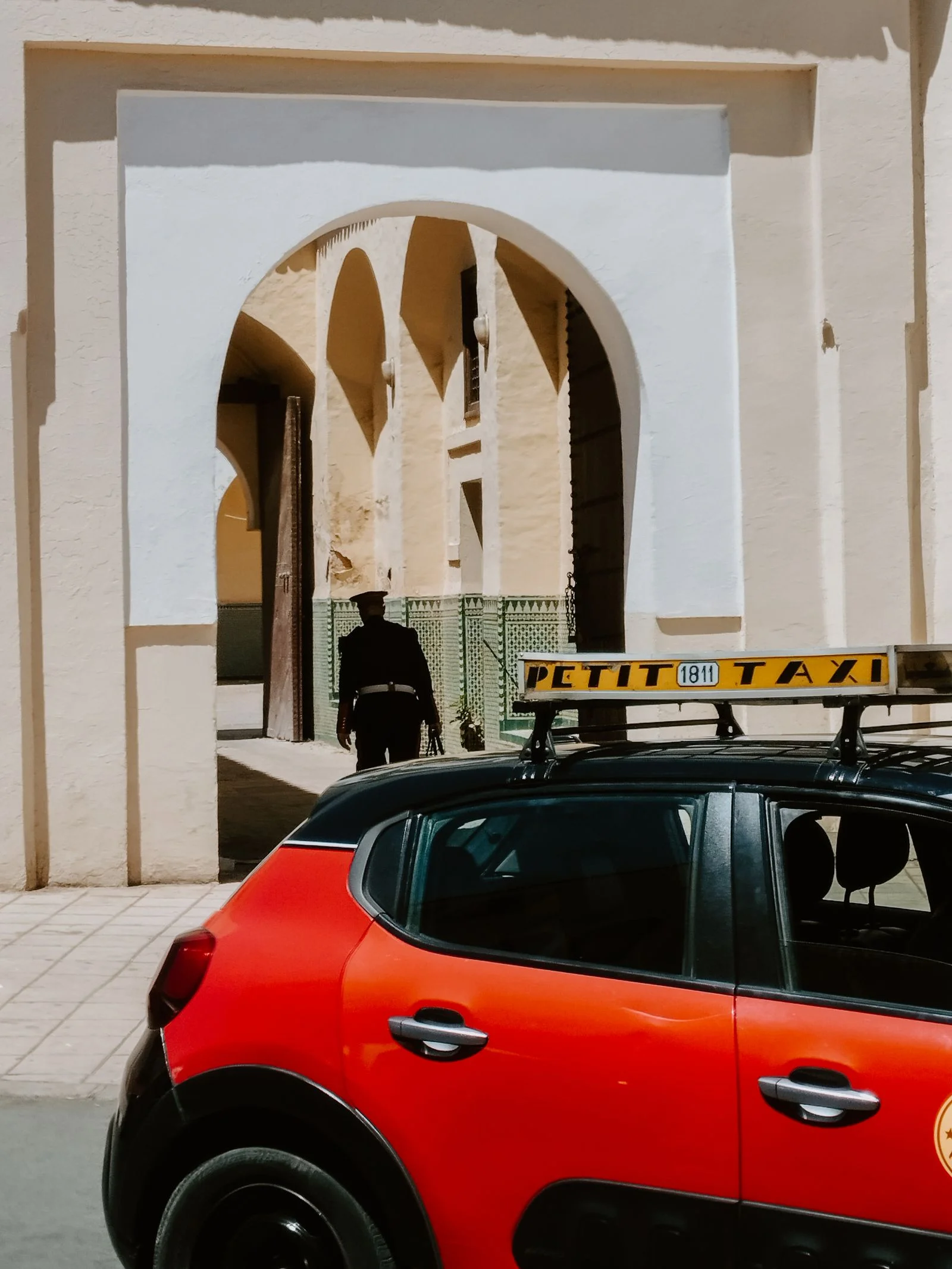 Red petit taxi driving through the historic streets of Fes